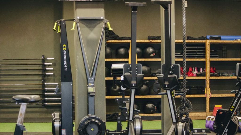 Modern gym with exercise equipment including rowing and ski machines, weights, and ropes.