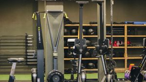 Modern gym with exercise equipment including rowing and ski machines, weights, and ropes.
